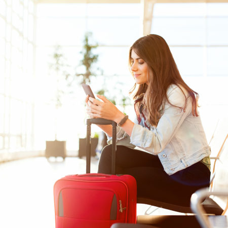 woman waiting in airport with luggage, phone, holiday traveling